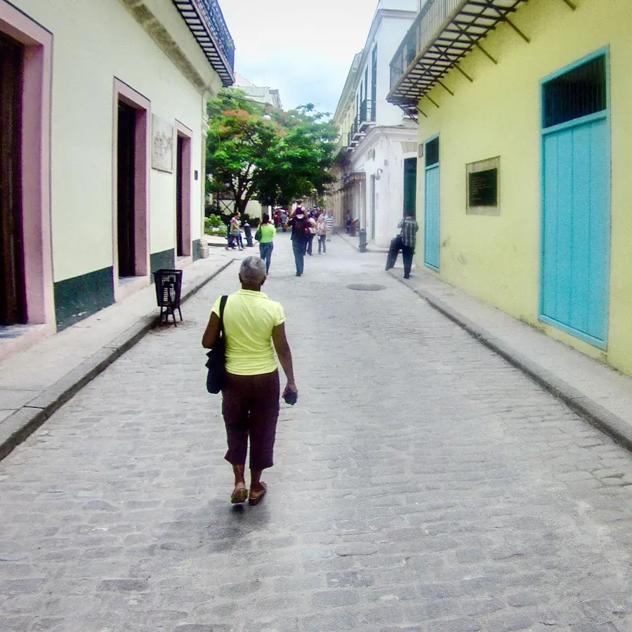 Mujer caminando por una calle empedrada entre casas de colores en La Habana