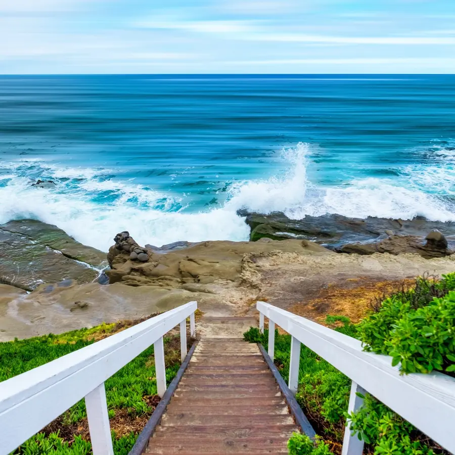 Escalera de madera con barandales blancos que baja hacia el mar y lleva la mirada al horizonte