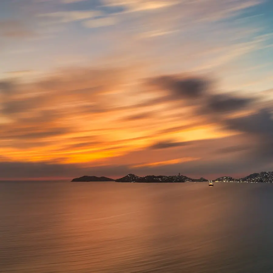 Atardecer naranja sobre el mar, con las nubes suavizadas por una exposición larga