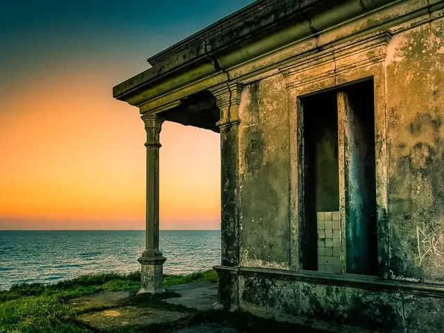 Casa en ruinas frente al mar durante un atardecer anaranjado